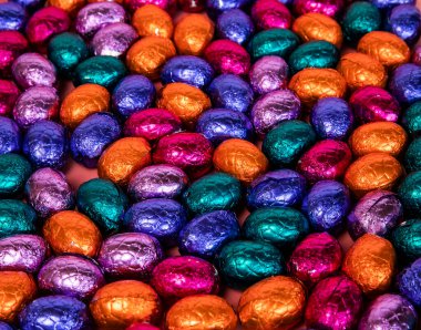 Pile of shiny wrapped chocolate Easter eggs, in colors red, blue and golden,green and purple. Festive Easter concept, top view pink background Happy easter close-up candy sweets concept stack