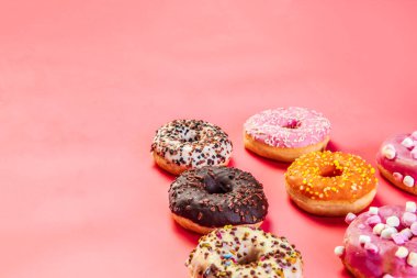 Doughnuts with multicolored glaze laid out in two rows on trendy pink background. Doughnuts are traditional sweet pastries. Copy space for text. top view