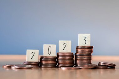 wooden cube year 2023 on top stack of coins with sky blue background and copy space. saving money and financial plan concept for investment in new year 2023. close up