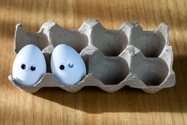 厨房桌上放着有机鸡蛋的纸盒里的白色鸡蛋上挂着滑稽的脸 大大的动画眼睛紧闭着 食物和复活节的概念 关门了 — 图库照片