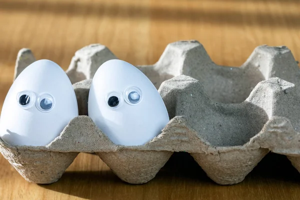 Funny faces on white eggs in carton box with organic chicken eggs on kitchen table closeup big animation eyes. humor, food and easter holiday concept. close up