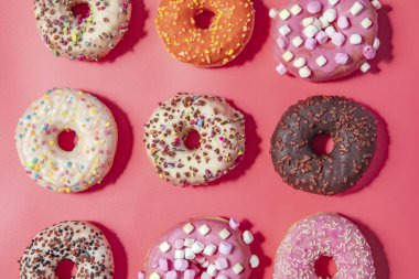 Donuts with icing on pastel pink background. Sweet donuts. top view assorted with various chocolate glazed and sprinkles, sugar sweets concept candy