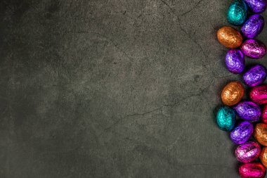 Delicious chocolate easter eggs ,sweets on dark black background,easter concept top view copy space wrapped colorful Happy Easter