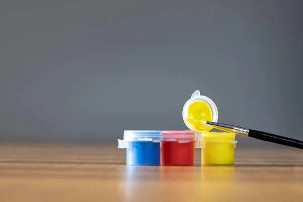 Artist paint brush with colorful paint on wooden table with gray background, copy space blue, red and yellow close up