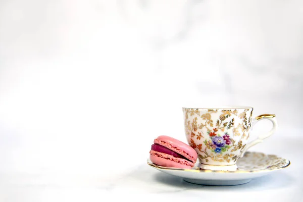 traditional English tea, high tea with vintage porcelain tea cup and pink macarone on white background, copy space pastel colored macaron sweets