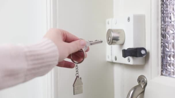 女性の手は家のフロントドアロックに家の鍵を入れ 女性はフロントドアのロックを開くために銀の鍵を使用して 白い木製のドアはロックされた家 セキュリティを開き 4Kを保存します — ストック動画