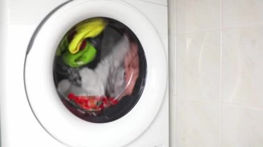 washing colored clothes in washing machine. automatic washer in operation, rotation multicolored things through glass door. laundry washing dryer and washing machine spinning rotate
