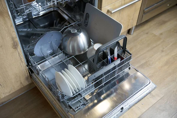 Stack of dirty dishes in dishwasher needs to be cleaned, open door with plates and dishes high angle view close up
