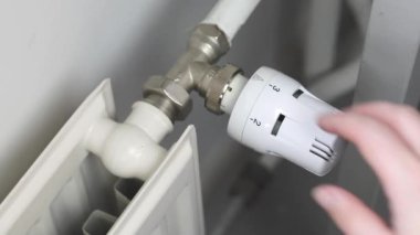 Woman turns off the heating by setting the thermostat of the central heating radiator to the minimum mode of maintaining the temperature in the room, number zero, saving money energy and gas crisis