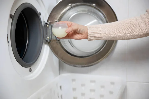 女用手把洗涤剂倒入量杯中 白色现代化房间里的洗衣机和衣服都关门了 — 图库照片