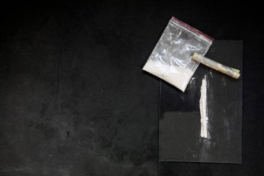 Cocaine powder lines, rolled banknote and drugs in plastic bag pocket on black glass surface background, top view. Drug addiction concept dark