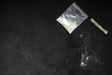 Cocaine powder lines, rolled banknote and drugs in plastic bag pocket on black glass surface background, top view. Drug addiction concept dark