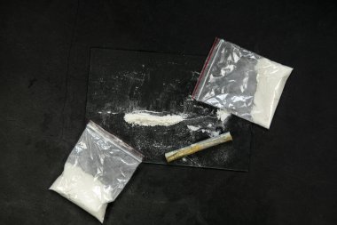 Cocaine powder lines, rolled banknote and drugs in plastic bag pocket on black glass surface background, top view. Drug addiction concept dark