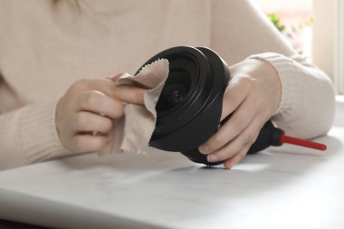 female photographer cleaning dslr fisheye camera lens with microfiber cloth, wipes dust of camera lens close up clipart