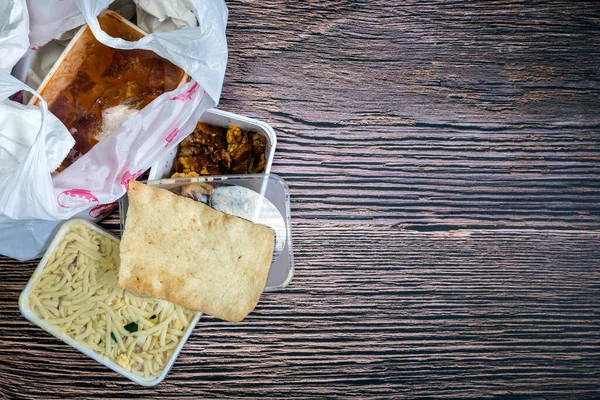 Chinese takeaway food selection in plastic bag. Bami, babi pangang, crispy shredded beef, sweet and sour chicken, krupuk top view on wooden table copy space. Food delivery Fast food