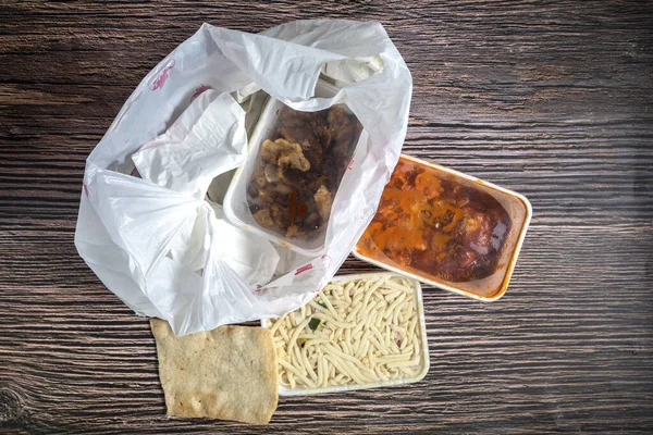 Chinese takeaway food selection in plastic bag. Bami, babi pangang, crispy shredded beef, sweet and sour chicken, krupuk top view on wooden table copy space. Food delivery Fast food