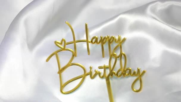 白いサテンの背景にハッピー誕生日のテキスト署名のトッパースティック 輝く金 お祭り お祝いの概念運動 — ストック動画