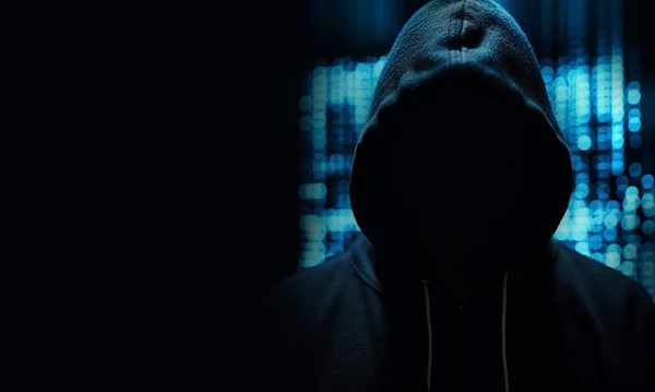 Hacker wearing black hoodie with blue neon lights on background, broke the security in the system.The dangers of digital thieves,unknown person with copy space danger