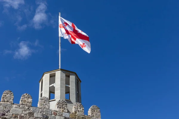 Georgian national flag (five-cross flag) waving on the wind against clear blue sky at the top of ancient watchtower of Akhaltsikhe (Rabati) Castle, Georgia.