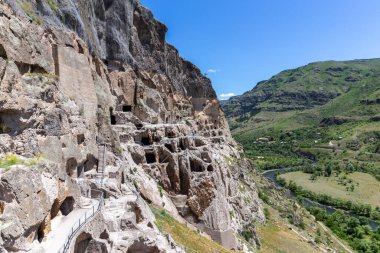 Vardzia cave monastery complex in Georgia, mountain slope with caves, tunnels and dwellings carved in the rock, Kura river valley in the background.