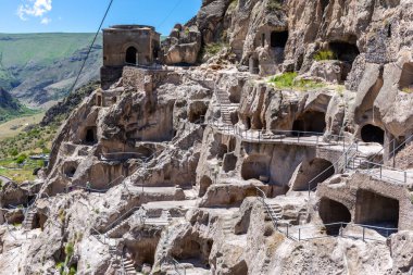 Vardzia cave monastery complex in Georgia, mountain slope with caves, tunnels and dwellings carved in the rock, bell tower building in the background. 