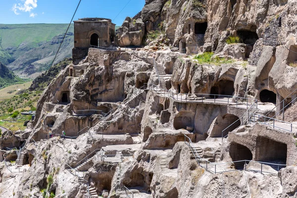Vardzia cave monastery complex in Georgia, mountain slope with caves, tunnels and dwellings carved in the rock, bell tower building in the background. 