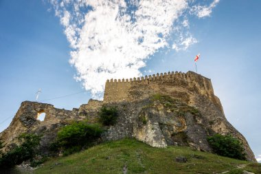 Surami fortress in Georgia, ruins of medieval castle at the top of a hill with Georgian national flag on defense wall, blue sky, low angle view.