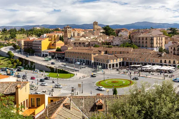 stock image Segovia, Spain, 03.10.21. Segovia cityscape with road, green roundabout, cars passing and narrow stone streets, medieval architecture, church bell towers, mountains in the background.