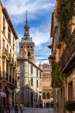 Segovia, İspanya, 03.10.21, Calle de Juan Bravo, Segovia 'da dar bir ortaçağ sokağı. Geleneksel bina cepheleri ve balkonları ve Iglesia de San Martin kilisesi arka planda yürüyen insanlar..