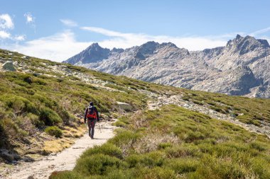 Sierra de Gredos dağlarındaki Plataforma de Gredos 'tan Laguna Grande Gredos Gölü' ne giden toprak yolda turist yürüyüşü, kuru kahverengi çimenler, sonbahar, İspanya.