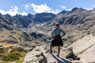 Sierra de Gredos 'taki Laguna Grande Gredos' a yürüyüş yapan kadın turist, yüksek kayalık dağlar ve arka planda göl, sonbahar manzarası.