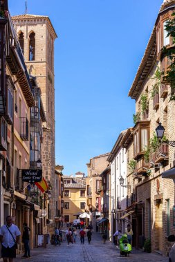 Toledo, İspanya, 08.10.21. Santo de Tome denilen dar bir ortaçağ kaldırımında dükkanlar, oteller, restoranlar, geleneksel balkonlar ve Santo Tome Mudejar Kulesi Kilisesi, yürüyen insanlar..