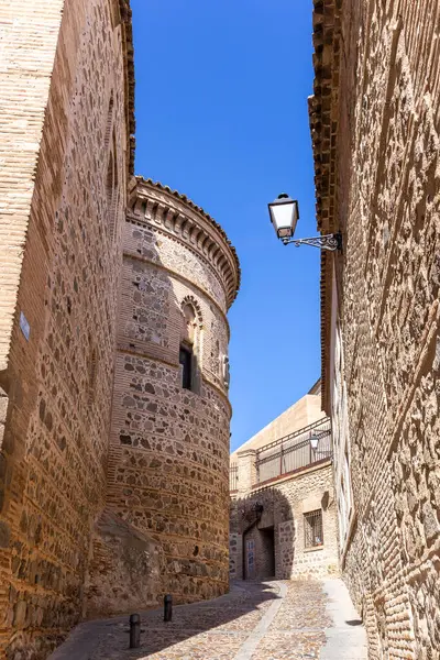 Narrow, stone cobbled medieval street with round facade of the Convent of Santa Ursula, stone walls, traditional balconies and street lamps. Translation: \