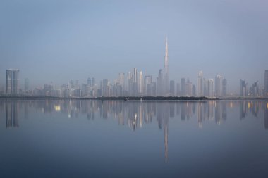 Dubai şehir merkezi gökyüzü manzarası Dubai Creek 'te yansımalı, soğuk renkler, gün doğmadan önce Dubai Creek Limanı gezinti güvertesinden görülüyor..