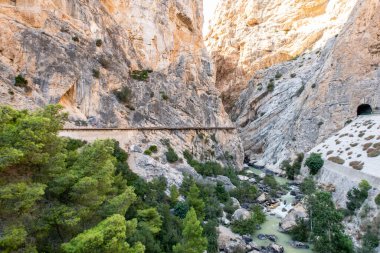 El Chorro 'nun dağ manzarası dar vadi, nehir ve El Caminito del Rey yürüyüş platformları uçurumun üzerindeki dikey kayalara bağlı, turistler yürüyor, İspanya.