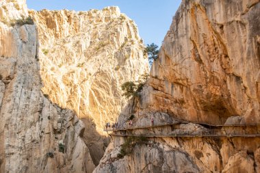 El Chorro 'nun dağ manzarası dar vadi, nehir ve El Caminito del Rey yürüyüş platformları uçurumun üzerindeki dikey kayalara bağlı, turistler yürüyor, İspanya.