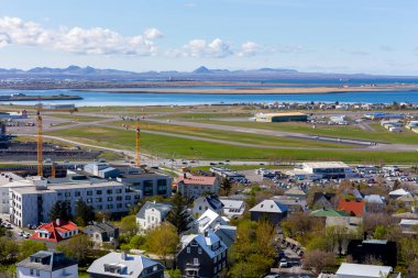 Reykjavik, İzlanda, 14.05.22. Reykjavik City iç havaalanı (RKV), pistli, terminal binalı, havalimanı altyapısı ve okyanuslu ve arka planda dağ manzaralı, güneşli bir gün.