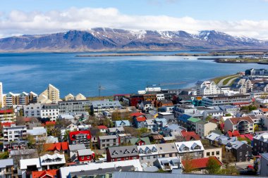 Reykjavik, İzlanda, renkli konut binaları, okyanus manzaralı ve Hallgrimskirkja kilise kulesinden görülen kar kaplı Esjan dağlık alanı manzaralı şehir manzarası.