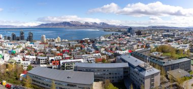 Reykjavik, İzlanda, renkli konut binaları, okyanus manzaralı ve arka planda Hallgrimskirkja kilise kulesinden görülen Esjan Dağı sıralı şehrin panoramik manzarası.