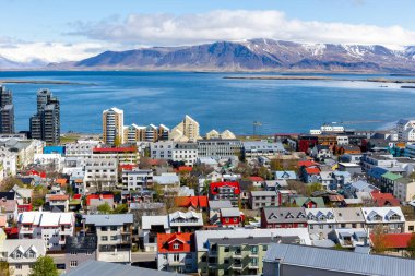 Reykjavik, İzlanda, renkli konut binaları, okyanus manzaralı ve Hallgrimskirkja kilise kulesinden görülen kar kaplı Esjan dağlık alanı manzaralı şehir manzarası.