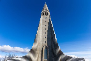 Hallgrimskirkja modernist church resembling basalt columns in Reykjavik, Iceland, modern belfry and wings against clear blue sky, symmetrical view. clipart