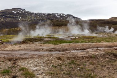 Haukadüler Vadisi, İzlanda 'daki Geysir Jeotermal Bölgesi' nde kaynayan kaplıcaları, sıcak su akıntıları ve arka planda dağlar var..