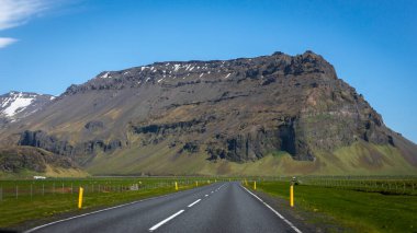 Güneşli bir günde, yeşil çayırlar ve arka planda kayalık dağlarla çevrili Güney İzlanda dağ manzarası..