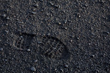 Siyah volkanik kumsalda tek ayak izi. Parlak volkanik taşlar ve Reynisfjara Kara Kum Sahili 'nde kül..