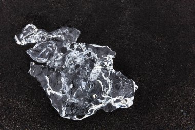 İzlanda 'da Diamond Sahili' nde volkanik siyah kumların üzerinde uzanan tek şeffaf buzdağı..