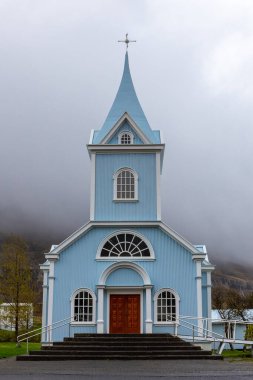 Seydisfjordur 'daki Mavi Kilise (Seydisfjardarkirkja), parlak mavi binanın dış görünüşü, arka planda sisli dağlar, İzlanda.