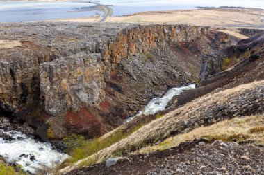 Flijotsdalshreppur, Doğu İzlanda 'daki Hengifossa nehir vadisinde arka planda kırmızı ve kahverengi kaya oluşumları, kayalıklar ve Lagarfljot buzul gölü bulunur..