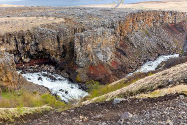 Flijotsdalshreppur, Doğu İzlanda 'daki Hengifossa nehir vadisinde arka planda kırmızı ve kahverengi kaya oluşumları, kayalıklar ve Lagarfljot buzul gölü bulunur..