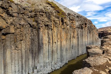 Studlagil Kanyonu (The Basalt Canyon) kahverengi buzul nehri ve dikey altıgen bazalt sütunlu vadi manzarası, İzlanda.