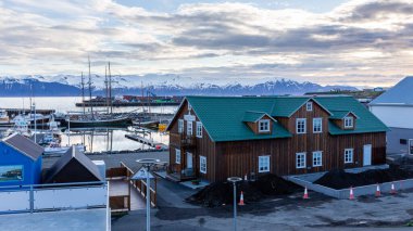 Husavik, İzlanda, 21.05.22. Liman manzaralı Husavik manzarası, geleneksel İzlanda mimarisi ve kar kaplı Viknafjoll ve Kinnarfjoll dağ sıraları arka planda, kutup gecesi.